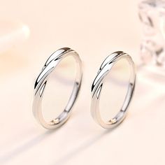 two silver rings sitting next to each other on top of a white surface with an ice cube in the background