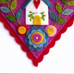 a felt decoration with flowers and a bird on it's back end, hanging from a wall