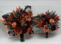 two bridal bouquets with orange and red flowers are on display against a white wall