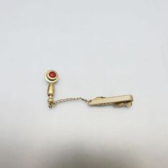 This very cool  goldtone metal tie clip or clasp is in very good condition with a stick pin attachment with a cranberry glass bead in a metal swirl . The stickpin measures 1 5/8ths inch high and  1/2  inches wide. It is attached to a tie clip by a 1 1/4 inch chain. It is marked HICKOK, USA on the back.   This will arrive in a lovely gift box for stellar gift giving or safe storage.  It would make a fabulous groomsman gift. If you like the older men's accessories, vintage costume jewelry, old sil Elegant Clip-on Brooches For Formal Occasions, Vintage Yellow Gold Pins For Formal Occasions, Antique Gold Pins For Formal Occasions, Classic Gold Pins For Formal Occasions, Ascot Ties, Groomsman Gift, Bolo Ties, Cranberry Glass, Safe Storage