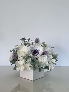 an arrangement of white and purple flowers in a square vase