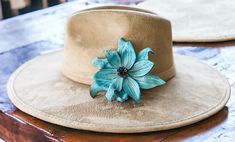 a hat with a blue flower on it sitting on top of a wooden table next to another hat