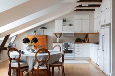 an attic kitchen and dining room with white cabinets, wood flooring, and exposed rafters