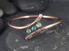 a copper cuff with three green beads on it sitting on top of a stone slab