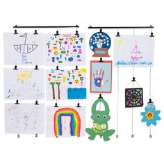 a group of children's artwork hanging from hooks on a white wall next to each other