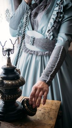 a woman in a blue dress talking on a phone next to a table with a lamp