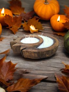 a wooden bowl filled with a candle surrounded by leaves and pumpkins on a table