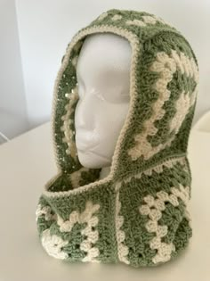 a white mannequin head wearing a green and white crochet hooded scarf