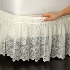 a person is holding the bottom of a white bed skirt with lace on it,