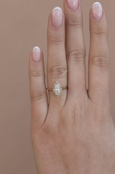 a woman's hand with a diamond ring on top of her finger, against a beige background