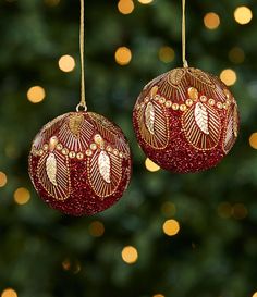 two red ornaments hanging from strings in front of a christmas tree