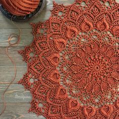 an orange crochet doily next to a ball of yarn on a wooden table