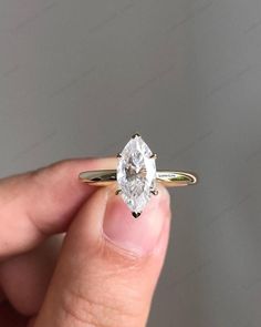 a woman's hand holding an engagement ring with a pear shaped diamond