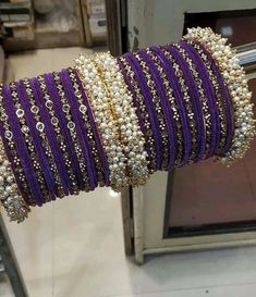 purple and gold bracelets are stacked on each other in a row with pearls around them