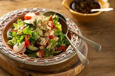 a salad on a plate with two spoons next to it