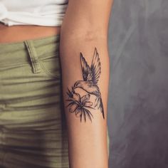 a woman's arm with a bird and flower tattoo on the left inner arm