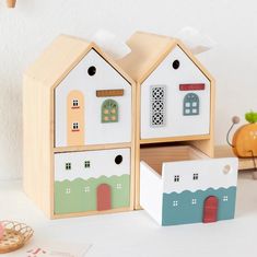 two wooden toy houses sitting next to each other on a white table with toys nearby