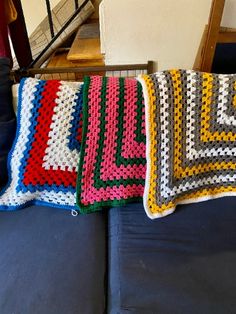 three crocheted squares are sitting on a couch next to a blue sofa cushion