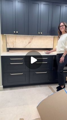 a woman standing in front of a kitchen counter with cabinets and drawers on the floor