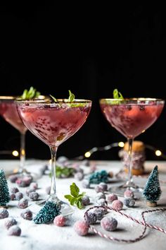 two glasses filled with pink and green drinks on top of a white table covered in snow