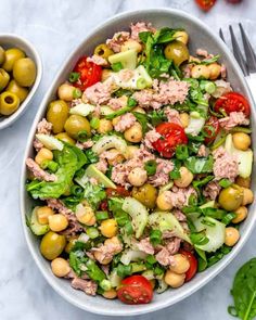 a bowl filled with salad and olives on top of a white table next to a fork