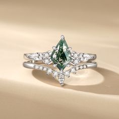 a green diamond ring with white diamonds around it on a beige surface in front of a tan background