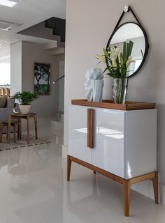 a vase with flowers on top of a white cabinet next to a mirror and table