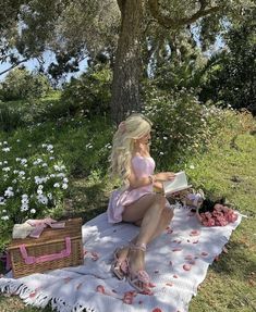 a barbie doll sitting on a blanket next to a picnic basket and flowers in the grass