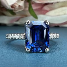 a blue and white diamond ring sitting on top of a table next to some flowers