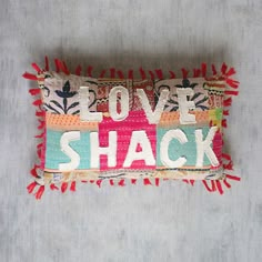 an embroidered love shack pillow sitting on top of a gray tablecloth covered surface with the words love shack written across it