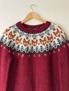 a red sweater with an orange and black design on the chest, hanging from a wooden hanger