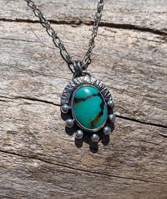 This oval Turquoise is set within a fine silver bezel, and surrounded and backed with sterling silver. Two lines of black and golden brown matrix run through the turquoise field like little trails.  Seven silver orbs adorn the bottom two-thirds of the setting. The remaining third is protected by a hammered and notched arcing sterling wall. The entire necklace has been oxidized and polished to enhance the details of the design. The chain is a textured long and short style and has been finished wi Turquoise Cabochon Chrysocolla Necklace, Southwestern Sterling Silver Oval Pendant Necklace, Sterling Silver Turquoise Necklace With Oxidized Finish, Unique Sterling Silver Cabochon Turquoise Necklace, Unique Turquoise Cabochon Necklace, Turquoise Gemstone Oval Pendant Jewelry, Southwestern Turquoise Necklace With Oval Pendant, Elegant Turquoise Necklace With Oxidized Finish, Southwestern Turquoise Oval Pendant Necklace