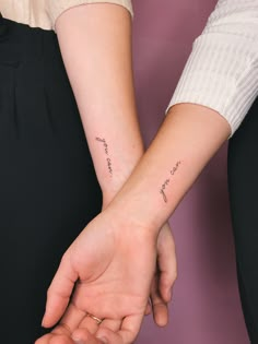 two people holding hands with small tattoos on their arms and the word love is written in cursive writing