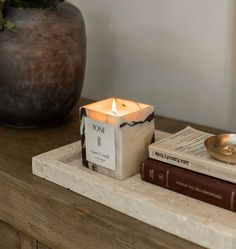 a candle sitting on top of a wooden table next to two books and a potted plant