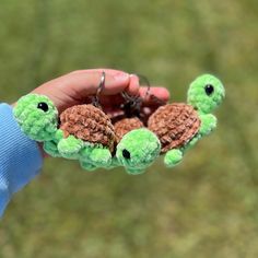 a person holding three tiny stuffed animals in their hands, one is green and the other is brown