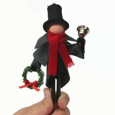 a hand holding a small doll with a red scarf and hat on it's head