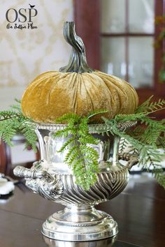 a pumpkin sitting on top of a silver vase filled with greenery and the words fall home tour