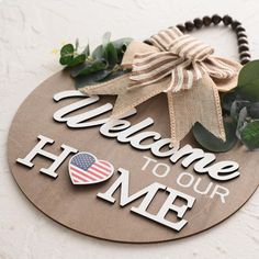 a welcome to our home sign with greenery and flowers on the front door hanger