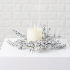 a candle is sitting on top of a table with silver leaves and snow flakes