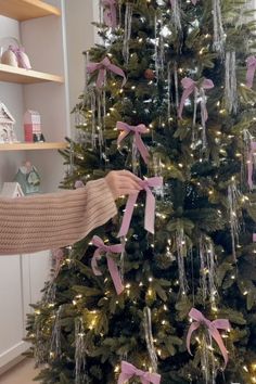 a woman is decorating a christmas tree with pink ribbons and bows on the top