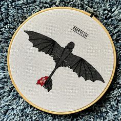 a cross stitched picture of a bat flying through the air with a red ribbon