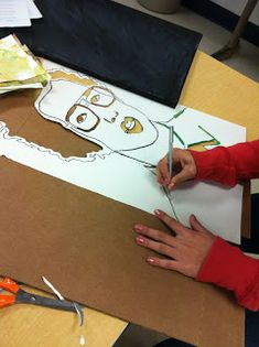 a person cutting out a paper face on top of a cardboard box