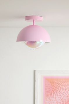 a pink light hanging from the ceiling in a white room with paintings on the wall