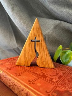 a wooden cross sitting on top of a red book next to a potted plant