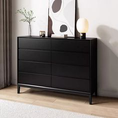 a black dresser sitting in front of a window next to a painting on the wall