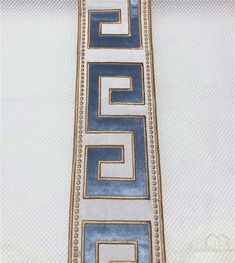 a blue and white tie with gold greek design on the side, hanging from a wall