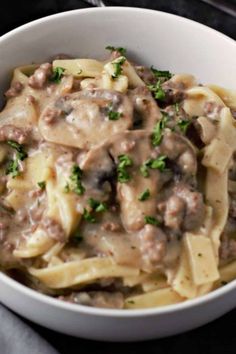 a white bowl filled with pasta covered in meat and gravy, garnished with parsley