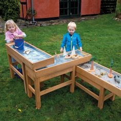 two children playing with sand and water in a garden area at the back of a red building