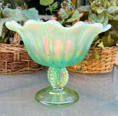 a green glass vase sitting on top of a table next to some potted plants