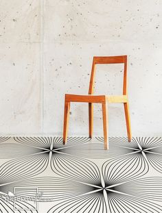 a wooden chair sitting on top of a floor next to a wall with an artistic pattern